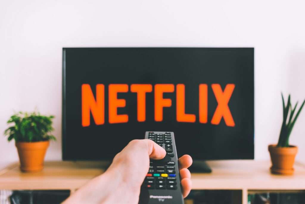 En TV med Netflix-logoen og en hånd med fjernkontrollen – illustrasjon til Netflix’ resultater for 2. kvartal 2026